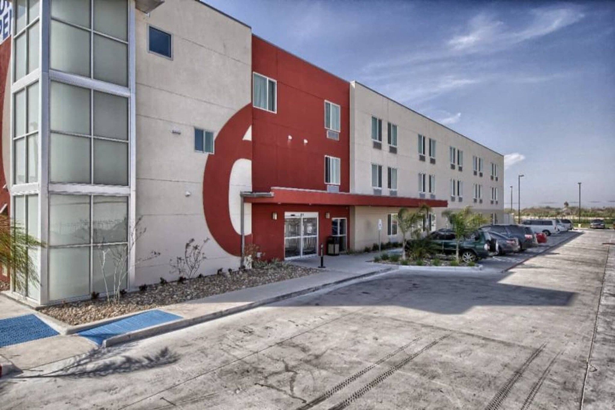 A modern building with a red and white facade, a parking lot, and a clear sky.
