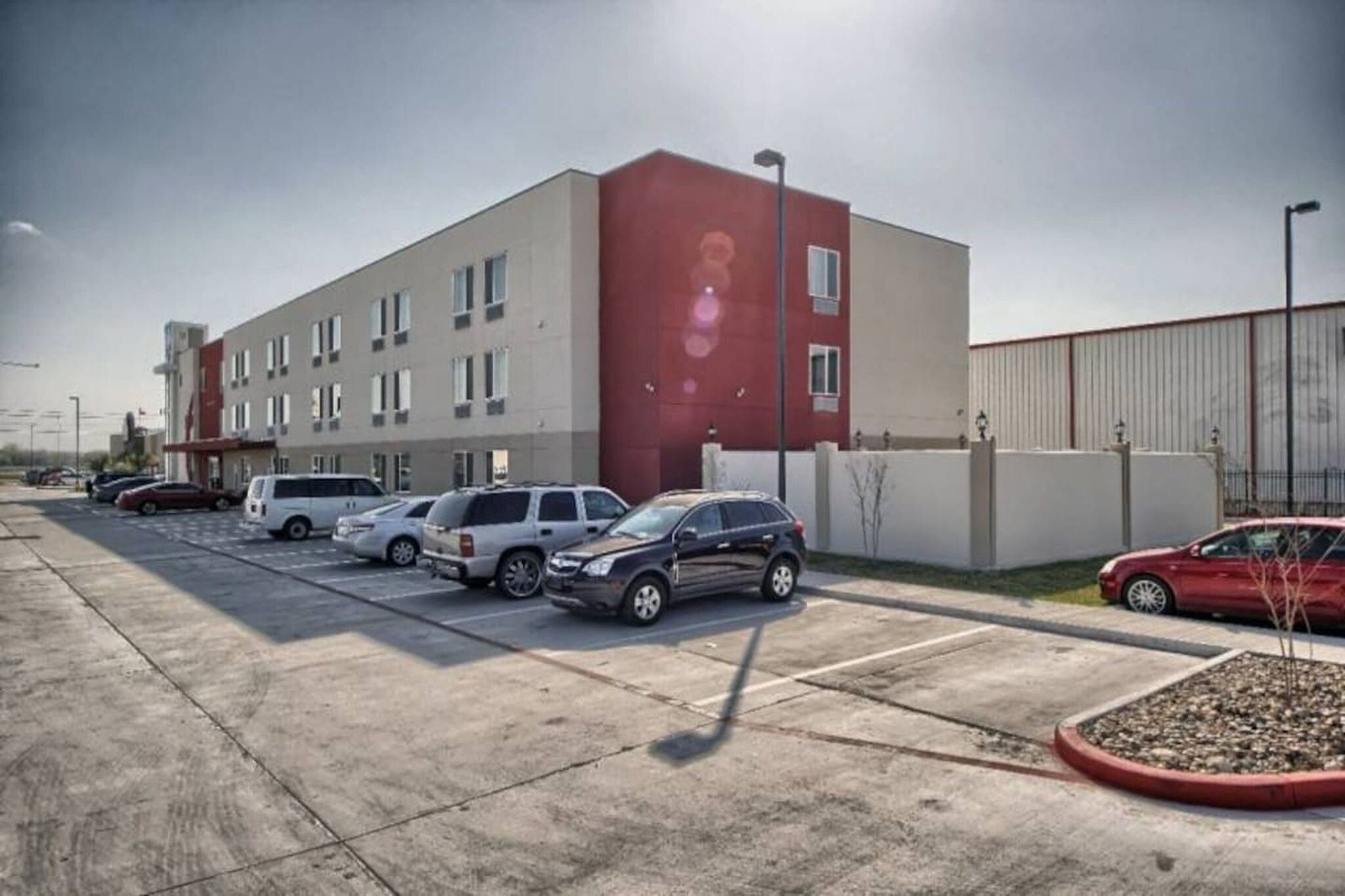 A parking lot with several cars, a building with a red section, and a clear sky.