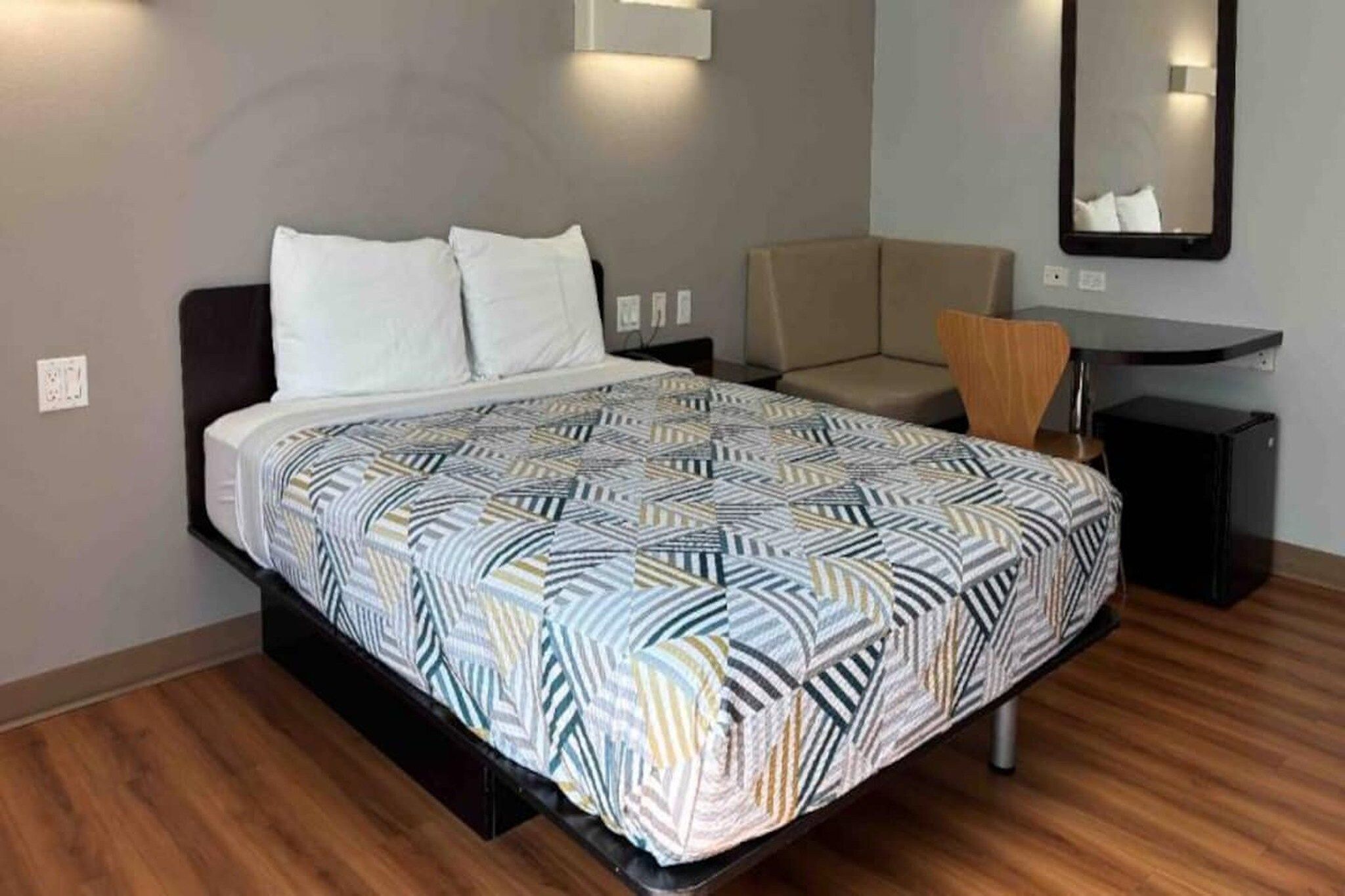 A bedroom with a bed, a desk, a chair, and a mirror.