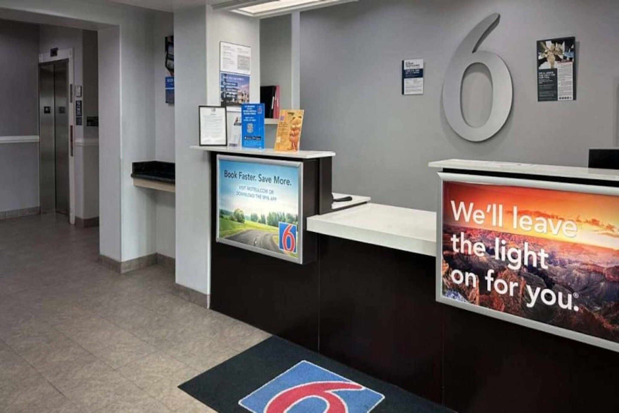 A reception desk with a large number '6' sign, a poster advertising a book app, and a sign that reads 'We'll leave the light on for you.'