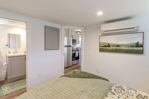 Quarto com cama, tapete verde, pintura e uma kitchenette ao fundo.