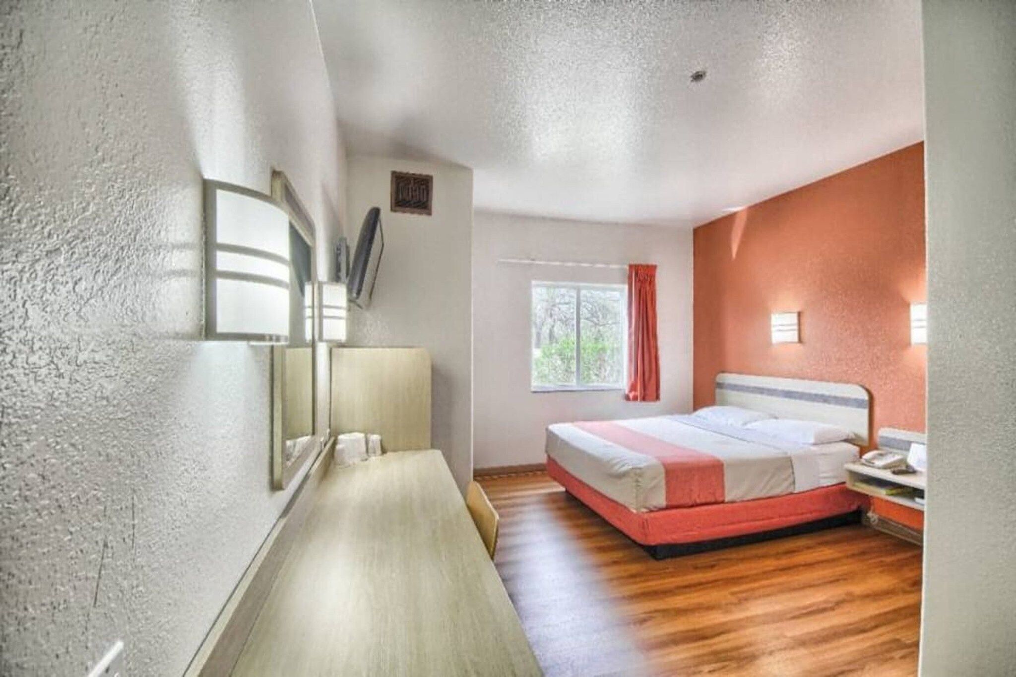 Une chambre à coucher avec un lit, une table de chevet, une lampe, une fenêtre et une vue sur les arbres.