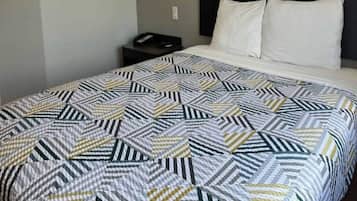 A bed with a geometric patterned bedspread, a bedside table with a phone, and a wall socket.
