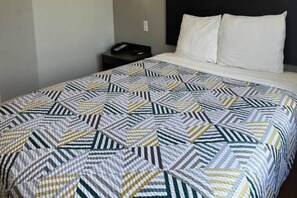 Una cama con una colcha de diseño geométrico, una mesita de noche con un teléfono y un enchufe de pared.