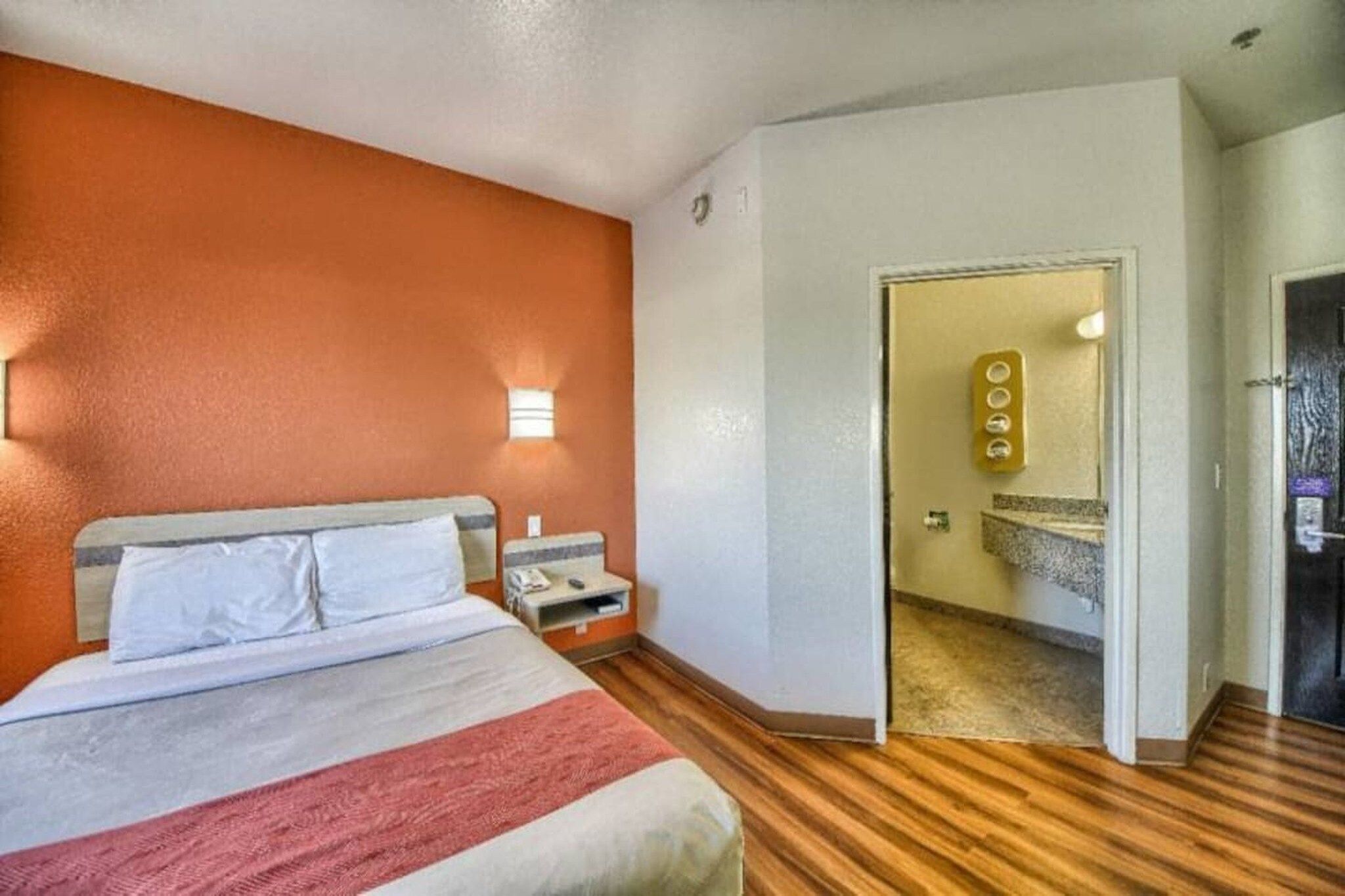 Una camera d'hotel con un letto, un comodino e un bagno visibile attraverso una porta aperta.