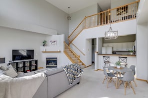 A modern living room with a grey sofa, a flat-screen TV, a fireplace, and a staircase leading to an upper level. - Shakopee Townhome Near Valleyfair & Mystic Lake (Shakopee)