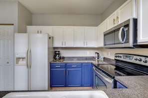 A kitchen with white cabinets, a blue countertop, a refrigerator, a microwave, a coffee maker, and an oven. - Shakopee Townhome Near Valleyfair & Mystic Lake (Shakopee)