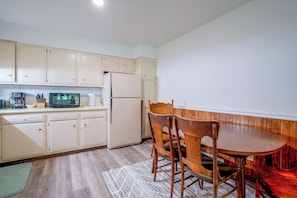 A compact kitchen with white cabinets, a refrigerator, a microwave, and a dining table with wooden chairs.