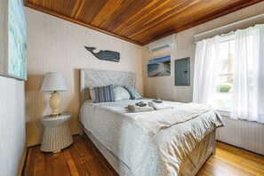 A bedroom with a bed, a bedside lamp, a wall-mounted air conditioner, and a window with curtains. - Steps to Shore! Old Orchard Beach Gem w/ Patio (Old Orchard Beach)