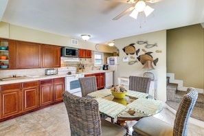 A kitchen with wooden cabinets, a microwave, a toaster, and a dining area with wicker chairs and a glass table. - Sun-Kissed Cottage: Lake Access, 14 Mi to Disney (Clermont)