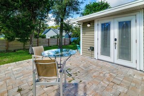 Une terrasse avec une table et des chaises en verre, un espace salon couvert et une maison avec une porte de garage.