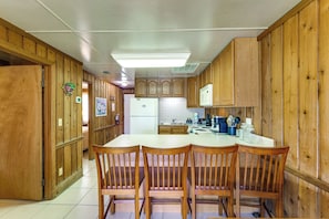 A kitchen with wooden cabinets, a central island, and a dining area with chairs. - Coconut Cottage: Community Amenities, Near Disney (Clermont)
