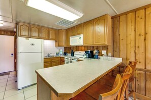 A kitchen with wooden cabinets, a refrigerator, a microwave, a stove, and a large island with chairs. - Coconut Cottage: Community Amenities, Near Disney (Clermont)