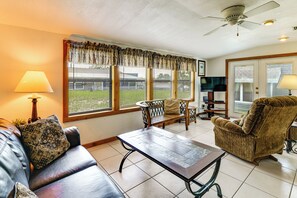 A living room with a sofa, armchair, and coffee table, a television, and a ceiling fan. - Coconut Cottage: Community Amenities, Near Disney (Clermont)