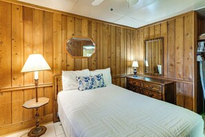 Un dormitorio con paredes de madera, una cama con ropa blanca, dos lámparas de noche, un aparador y un espejo.