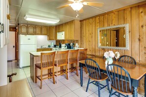 Una cocina con armarios de madera, un refrigerador blanco, un microondas, un fregadero y un comedor con mesa y sillas.