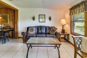 Ein Wohnzimmer mit Ledersofa, Couchtisch, Esstisch mit Stühlen und einem Fenster mit Jalousien.
