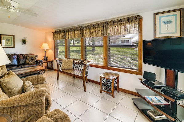 Una sala de estar con un sofá, un banco de madera, un televisor y una mesa con libros y dispositivos electrónicos.