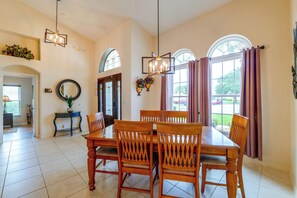 A dining area with a wooden table and chairs, a chandelier, and large windows with curtains. - Spacious 4BR w/ South-Facing Pool/Spa: Disney 11Mi (Clermont)