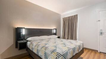 A hotel room with a bed, bedside table, and a door.