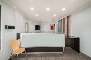 A reception area with a white reception desk, a single orange chair, a flat-screen TV mounted on the wall, and a colorful striped wall decoration. - 1 King Bed | Smoking, Kitchen (Laredo)