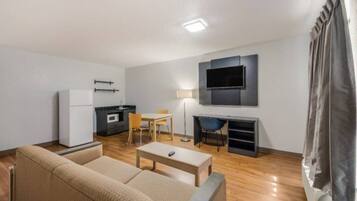 Una sala de estar moderna con un sofá, una mesa de centro, un televisor montado en la pared, una zona de comedor con una mesa y sillas, y una kitchenette con un microondas.