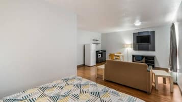 A modern hotel room with a bed, a sofa, a dining table, a TV, and a kitchenette.
