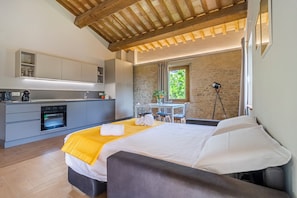 A modern bedroom with a bed, a small kitchenette, a dining table, and a stone wall.