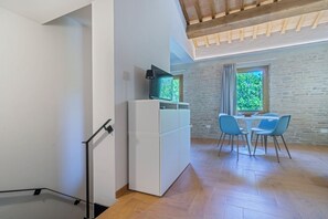 Una cocina moderna con armarios blancos, encimera negra y televisor empotrado. Hay un comedor con mesa y sillas, y una ventana con vistas a zonas verdes.