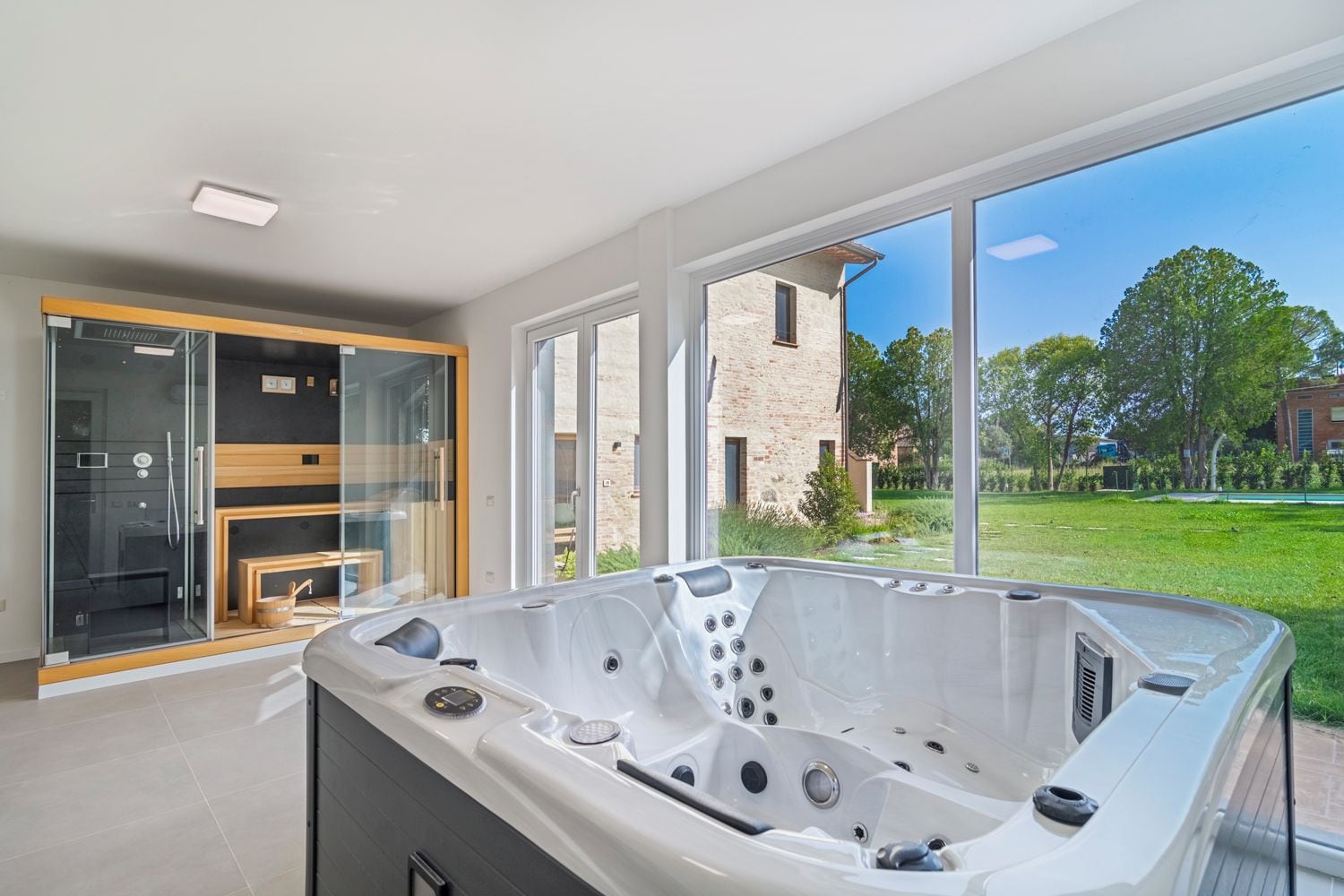 A modern bathroom with a large bathtub, glass shower enclosure, and a view of a brick building and greenery.