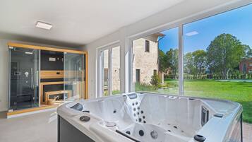 A modern bathroom with a large bathtub, glass shower enclosure, and a view of a brick building and greenery.