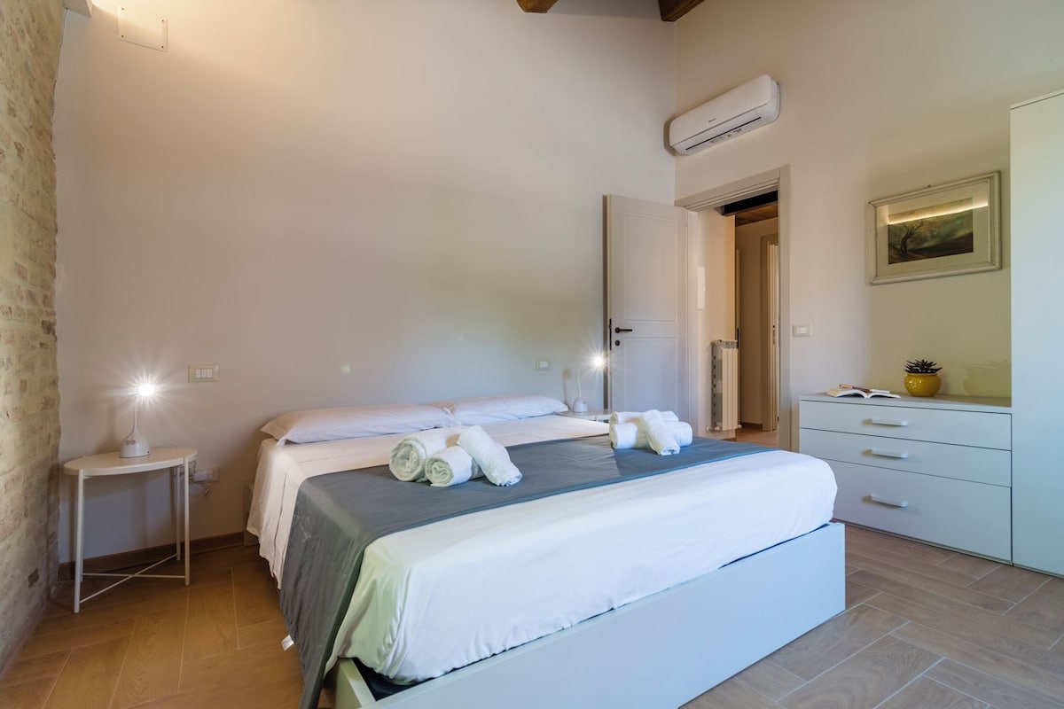 A hotel room with a bed, bedside table, lamp, air conditioning unit, and a dresser.