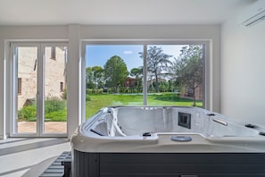 A modern bathroom with a hot tub, large windows, and a view of a garden and buildings. - Agriturismo Borgo Re (Deruta)