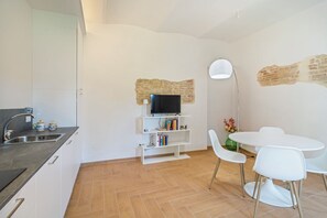 A compact kitchen with a built-in TV, white cabinets, and a dining area with a round table and chairs.