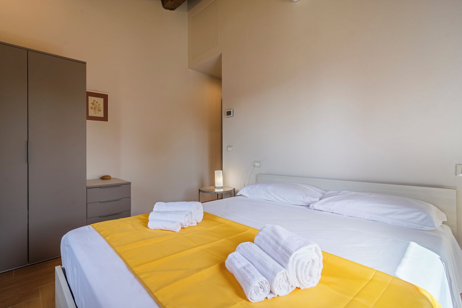 Una habitación de hotel con una cama, una mesita de noche, una lámpara y un armario.