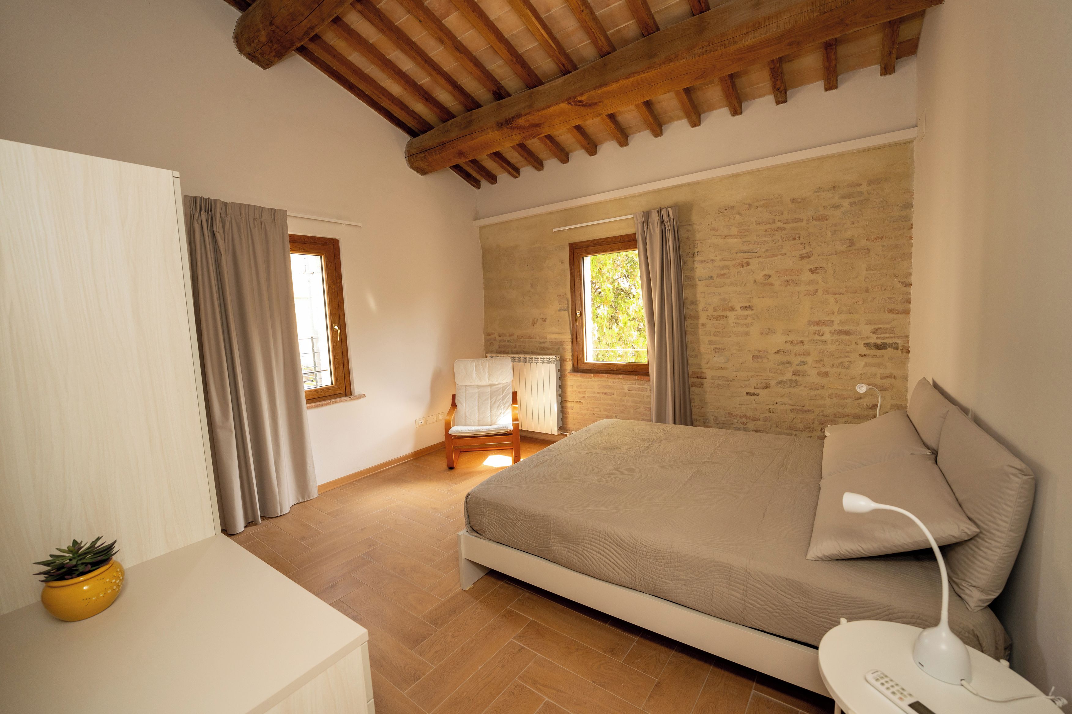 Un dormitorio con cama, una silla, una mesita de noche y una ventana.