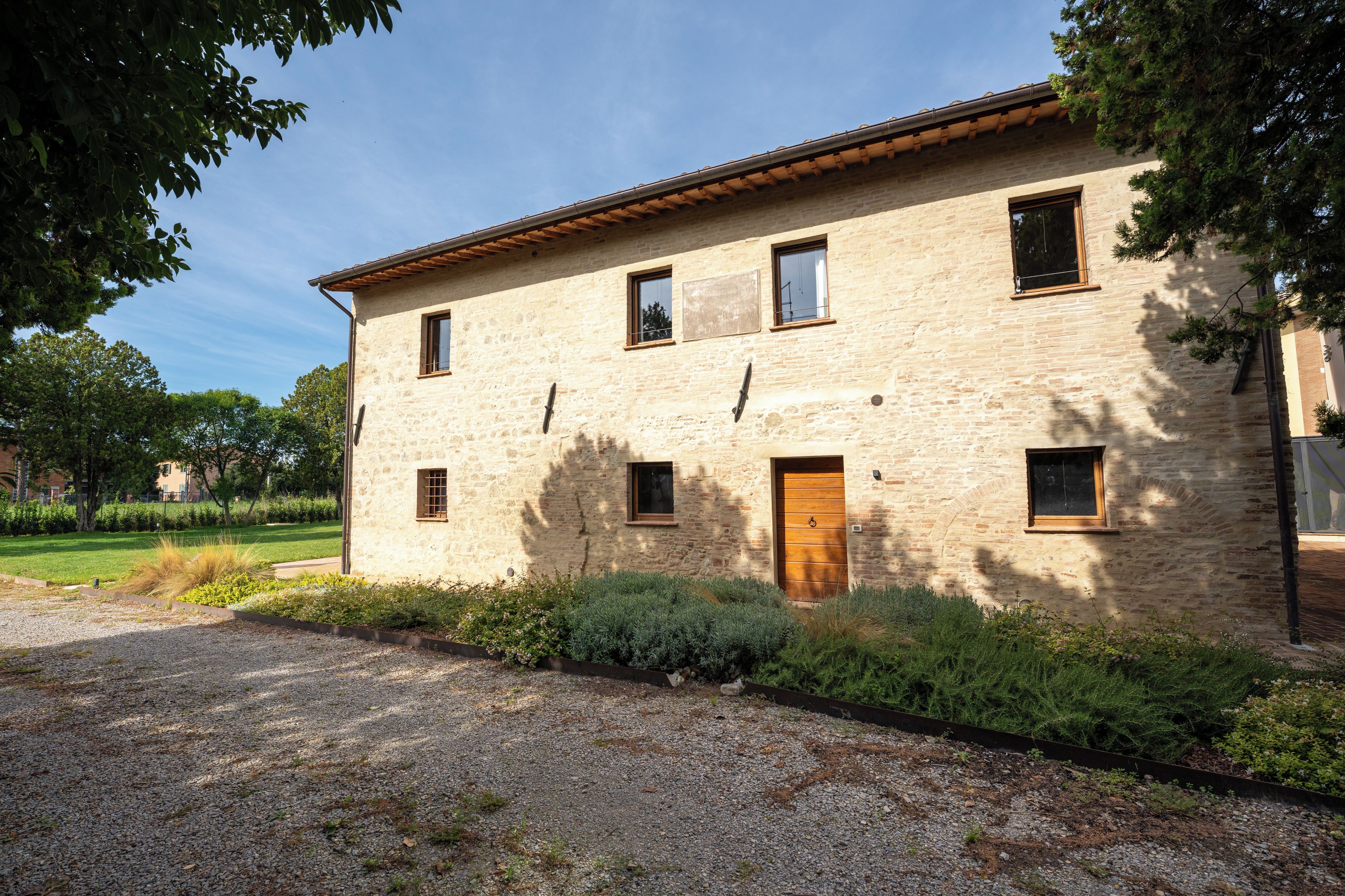 A stone building with a wooden door, multiple windows, and a gravel driveway.
