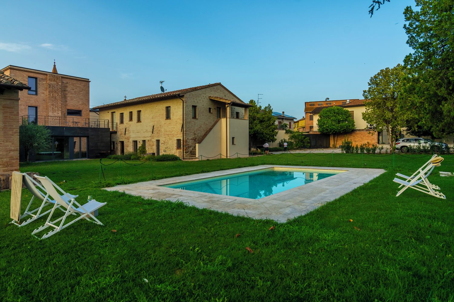 A swimming pool surrounded by a grassy lawn, with a few lounge chairs and a building in the background.