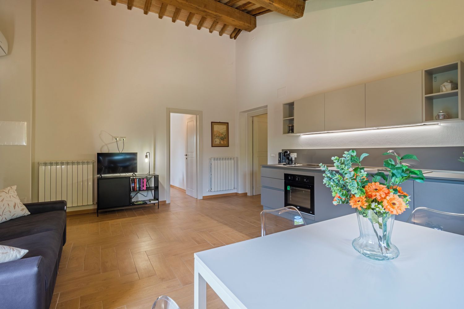 Un moderno salón con sofá, televisión y mesa de comedor con un jarrón de flores.