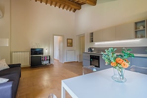 A modern living room with a sofa, a television, and a dining table with a vase of flowers. - Agriturismo Borgo Re (Deruta)