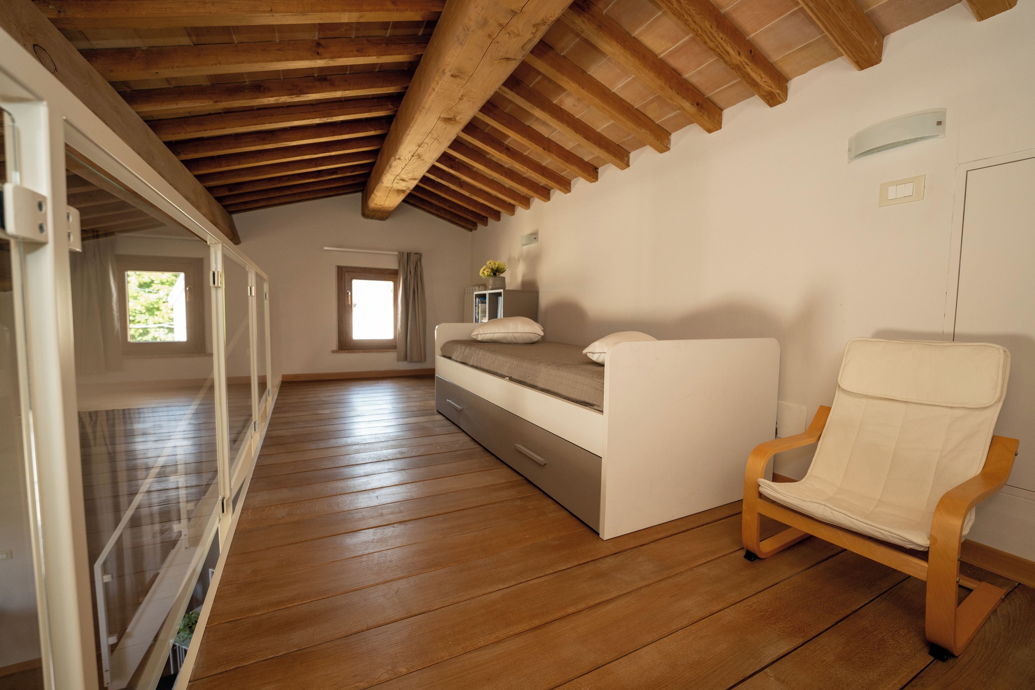 Un dormitorio con piso de madera, una cama, una silla y un ventanal.
