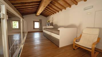 Un dormitorio con piso de madera, una cama, una silla y un ventanal.