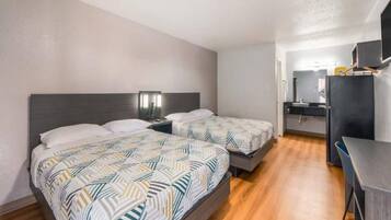 Quarto de hotel com duas camas, uma escrivaninha e uma cozinha compacta.