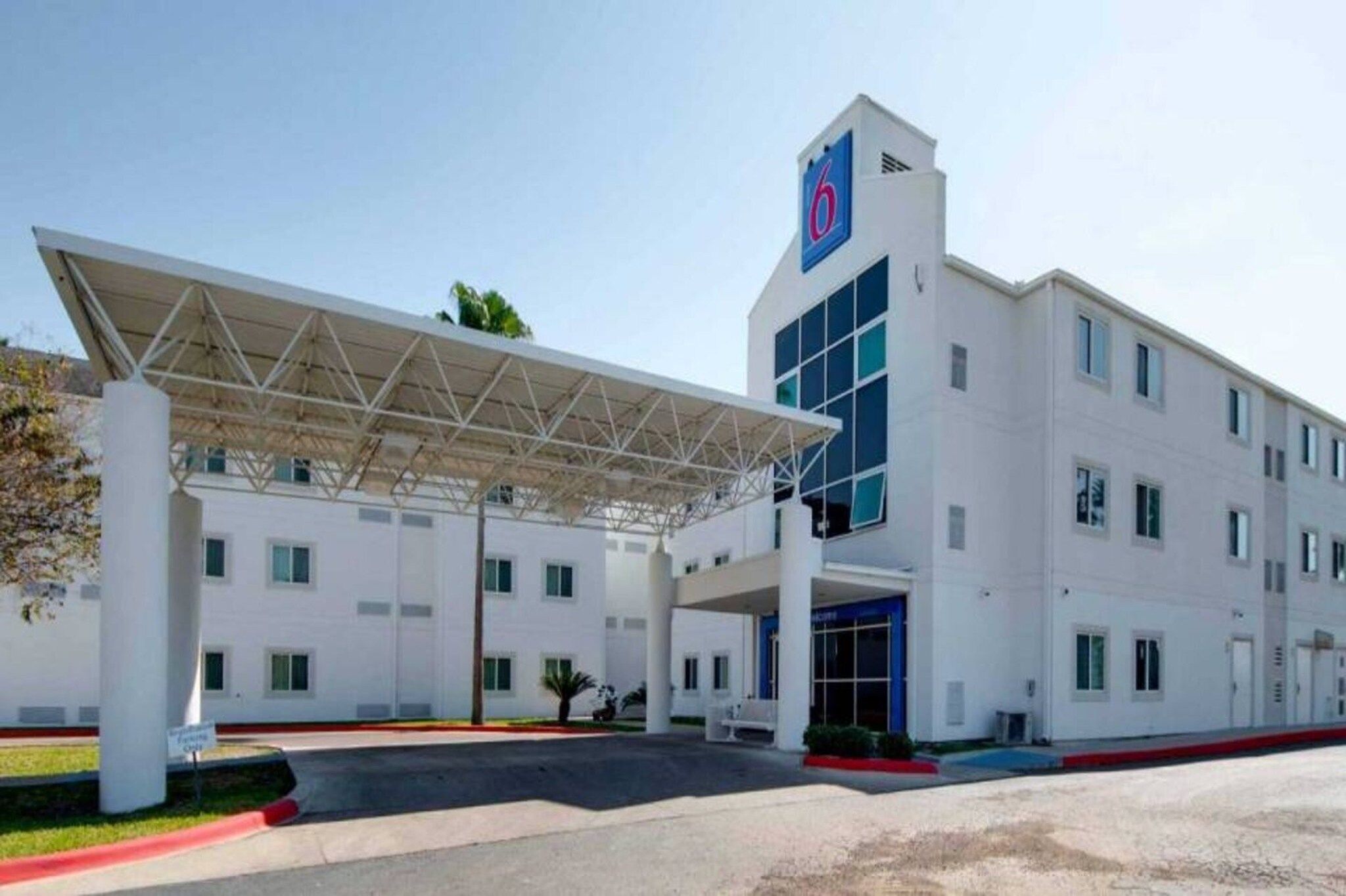 A hotel with a covered entrance, multiple windows, and a prominent '6' sign on the building.