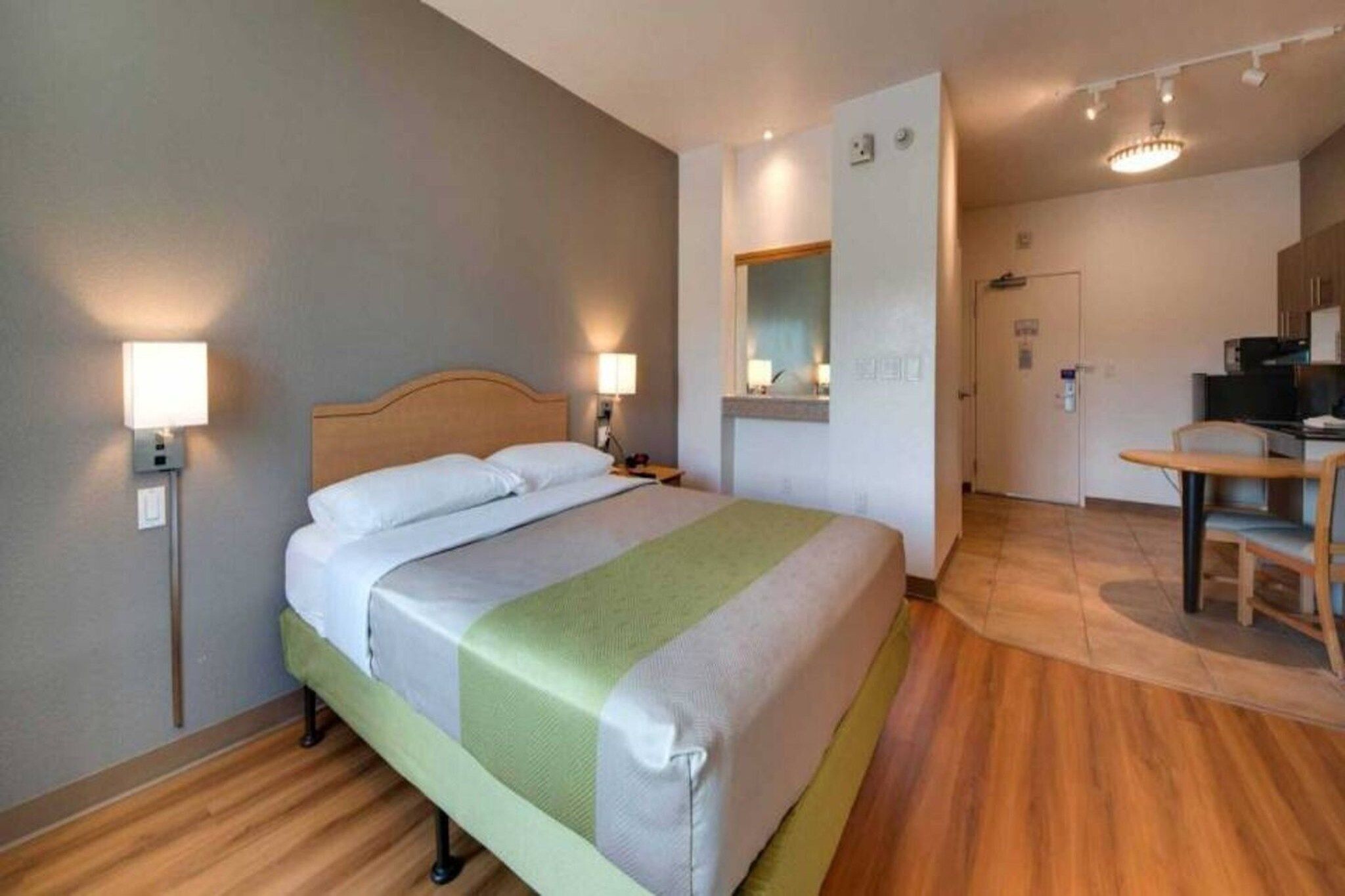 Et hotelværelse med seng, sengeborde, et spejl, et skrivebord og et tekøkken.