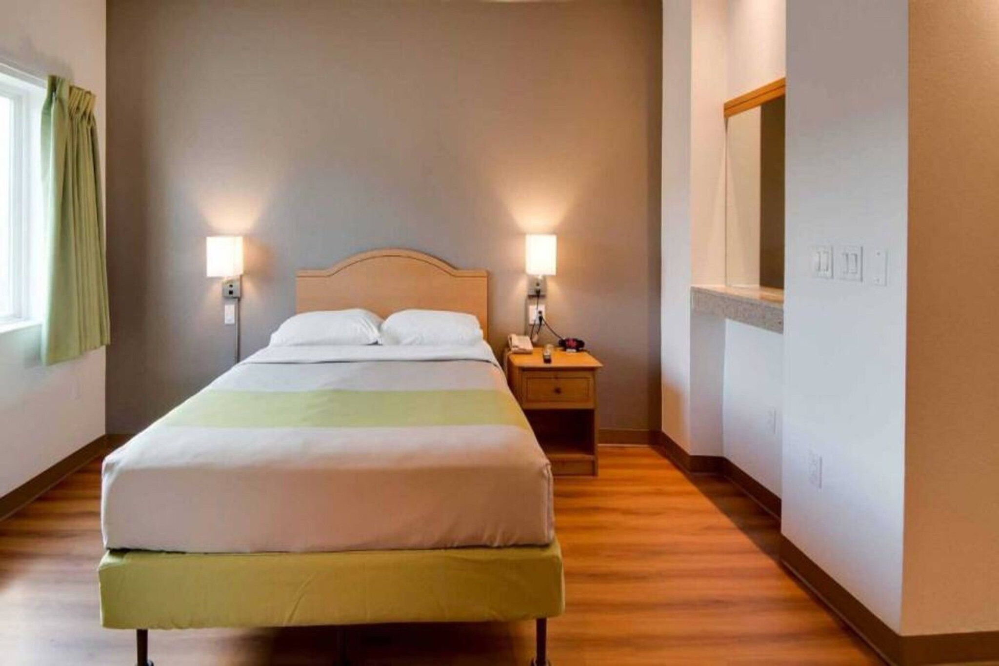 A hotel room with a bed, bedside lamps, a nightstand, and a mirror.