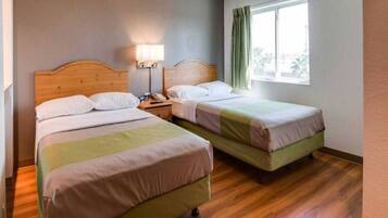 A hotel room with two beds, a nightstand with a lamp, and a window with curtains.