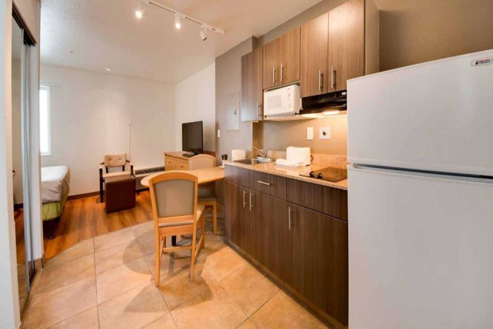 A compact kitchen with a refrigerator, microwave, and wooden cabinets. There is a dining area with a chair and a table.