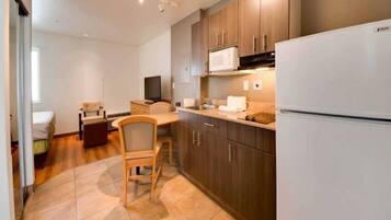 A compact kitchen with a refrigerator, microwave, and wooden cabinets. There is a dining area with a chair and a table.