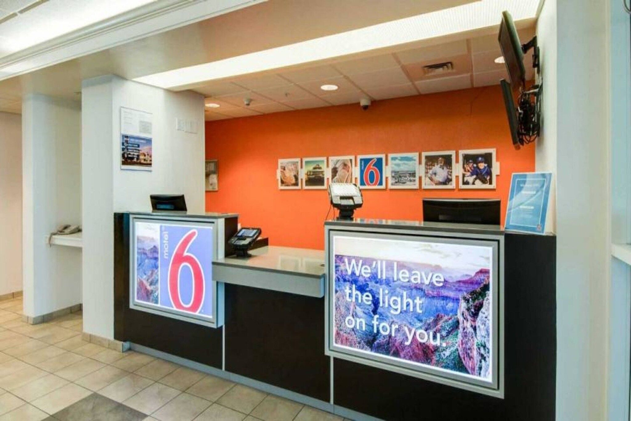 A hotel reception desk with a large number 6 sign, a digital display with a message, and a series of framed pictures on the wall.
